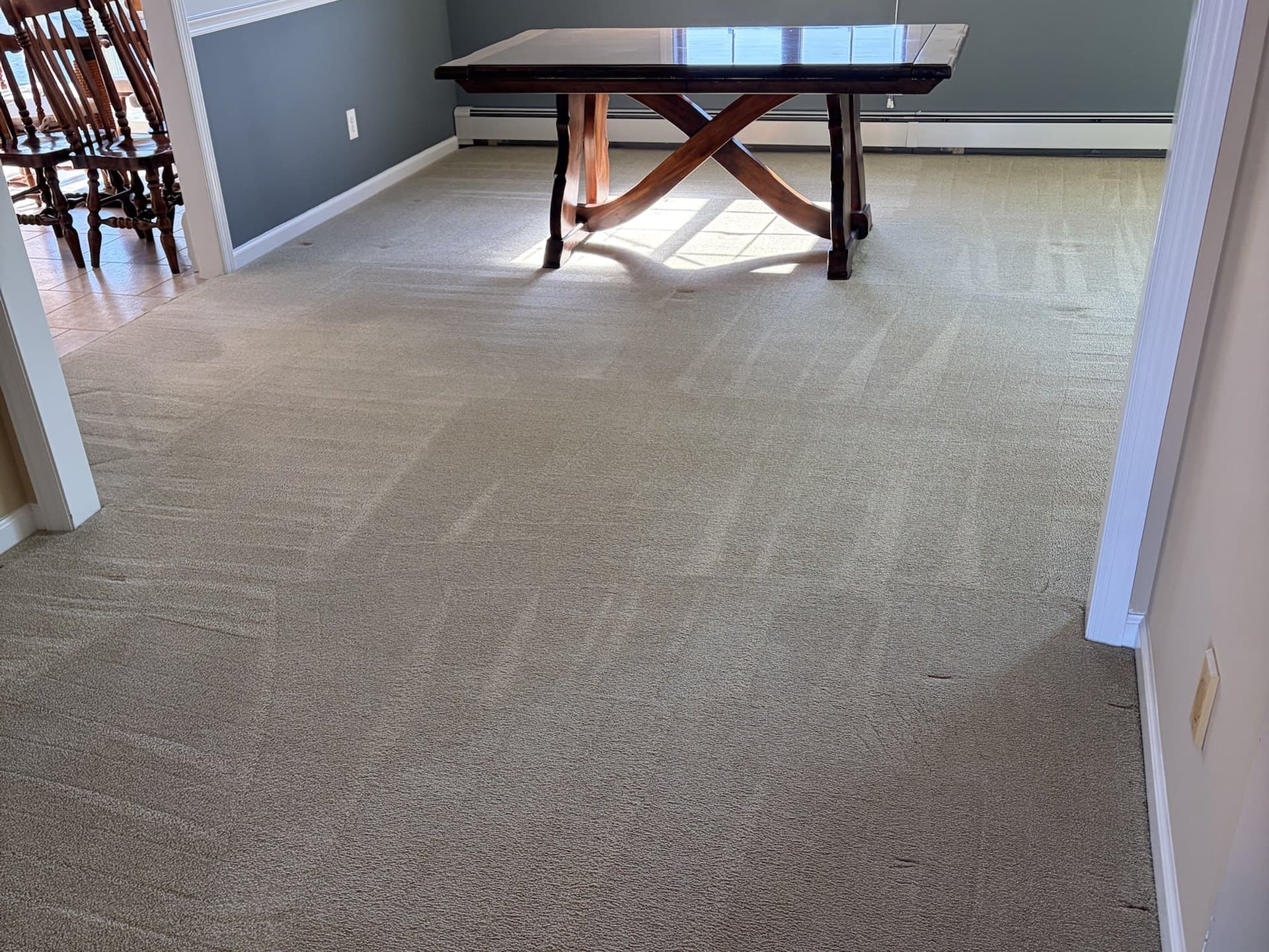 Cream dining-room carpet groomed in even rows around a trestle table, beside the same dining room's carpet dull and gray before cleaning