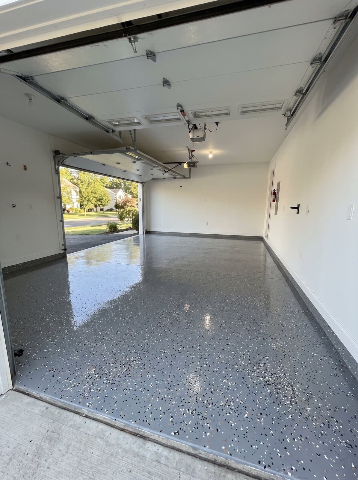 Glossy gray epoxy flake floor coating in a two-car garage with the door open to the driveway
